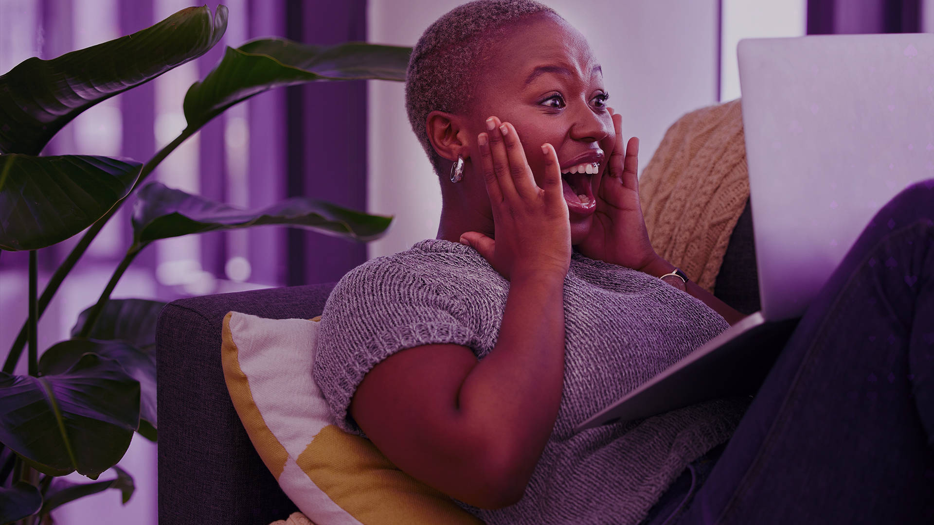Woman with hands to face, looking at laptop with excited expression.