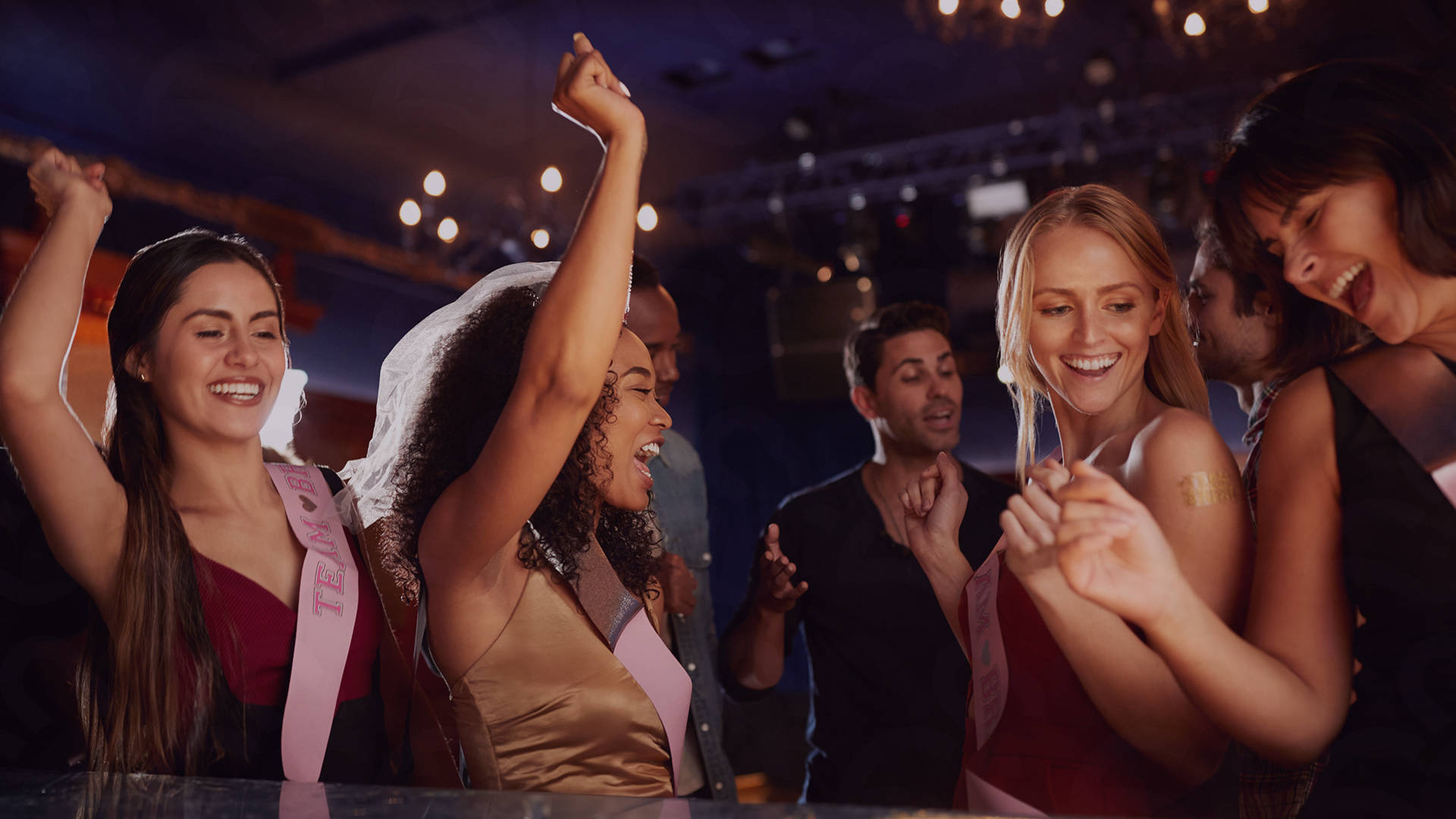 Group of women celebrating at a bar, wearing sashes.